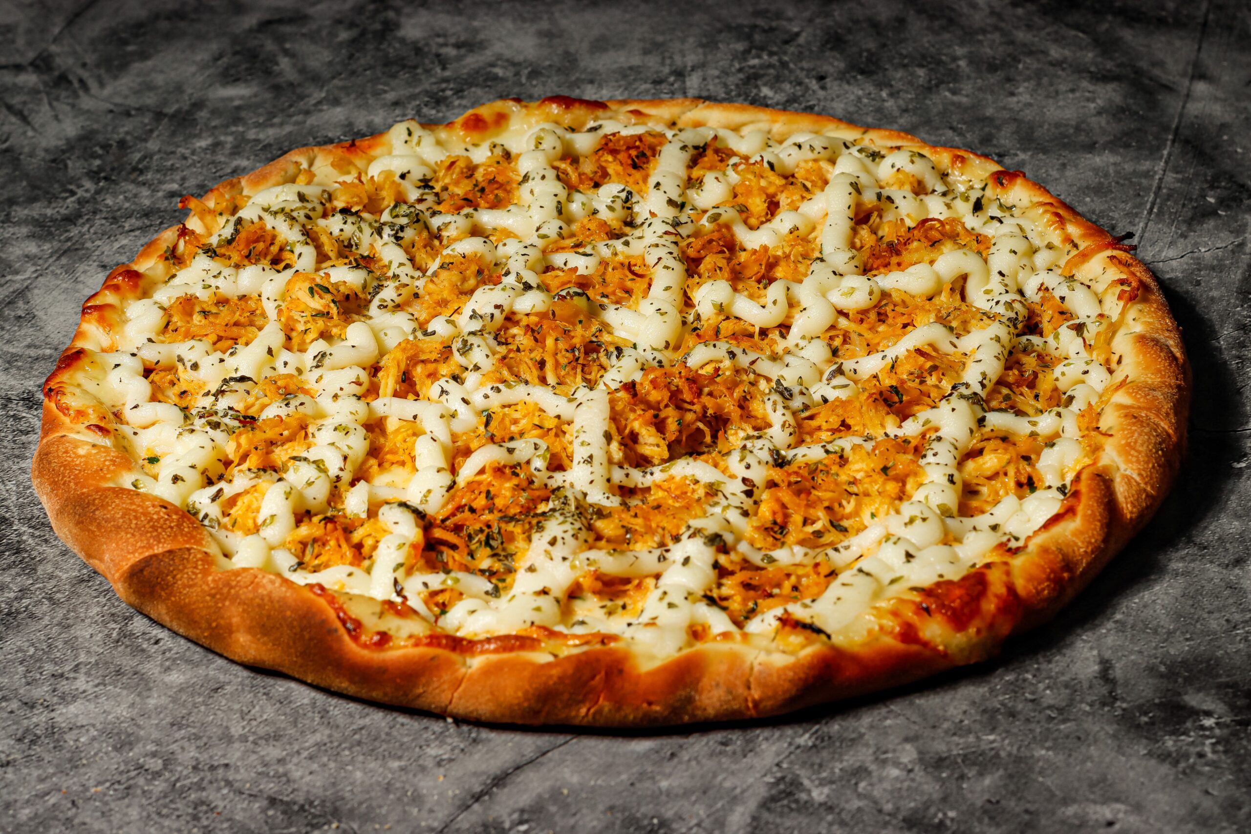 Close-up of a chicken pizza topped with herbs and cheese on a rustic surface.