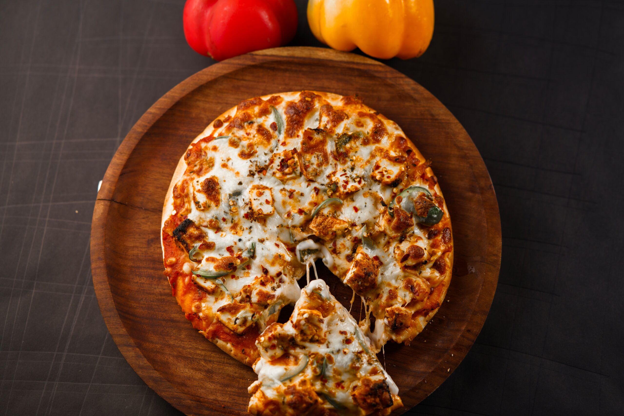A mouth-watering cheese pizza on a wooden board with vibrant bell peppers.