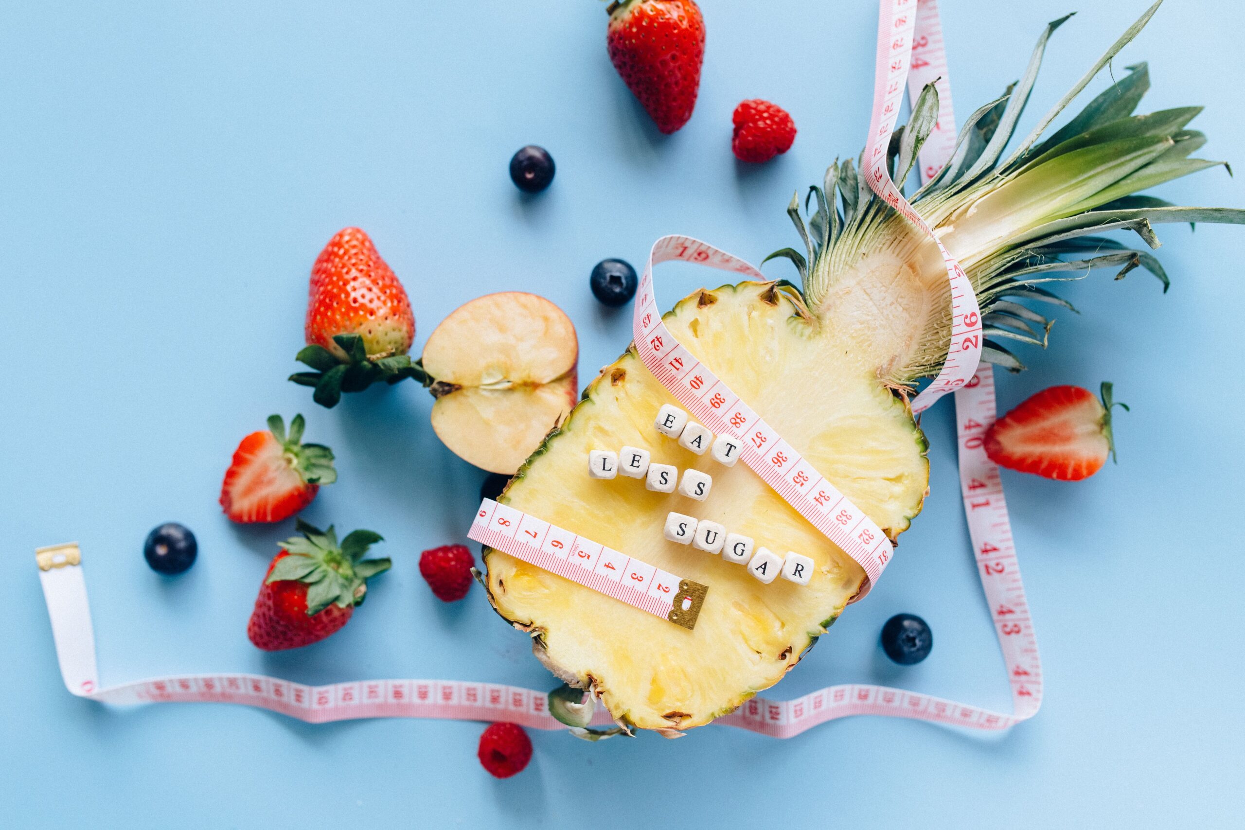 A sliced pineapple with berries and a tape measure on a blue background promoting healthy eating.